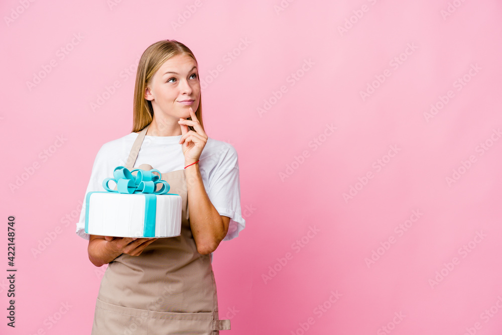 Young russian baker woman holding a delicious cake looking sideways with doubtful and skeptical expression. Young russian baker woman holding a delicious cake looking sideways with doubtful and skeptical expression.