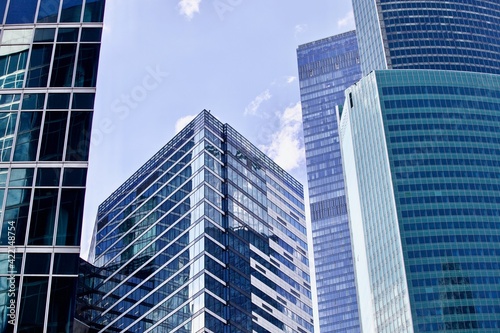 Office and residential skyscrapers against bright sun and clear blue sky close up. Reflections and glare on the glass facades of modern skyscrapers close-up. Modern buildings exterior design.  © ST-art