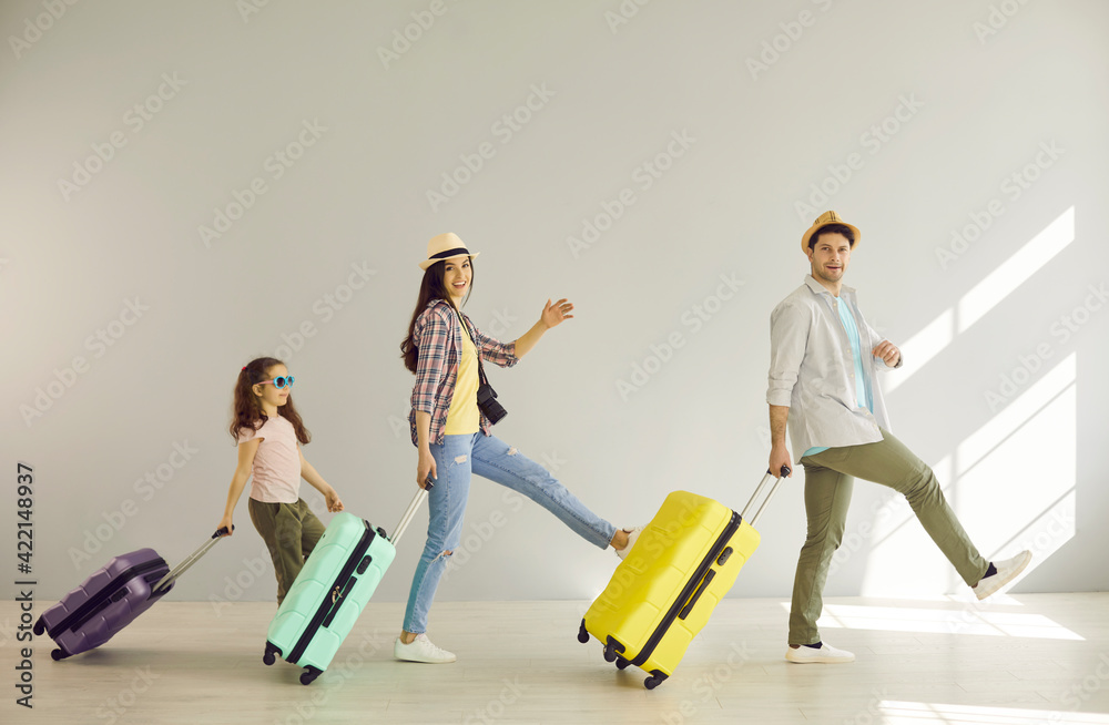 Naklejka premium Family goes on summer vacation. Cheerful mom, dad and their daughter have fun walking with suitcases along the gray wall. Concept of active family, travel and summer vacations. Banner.
