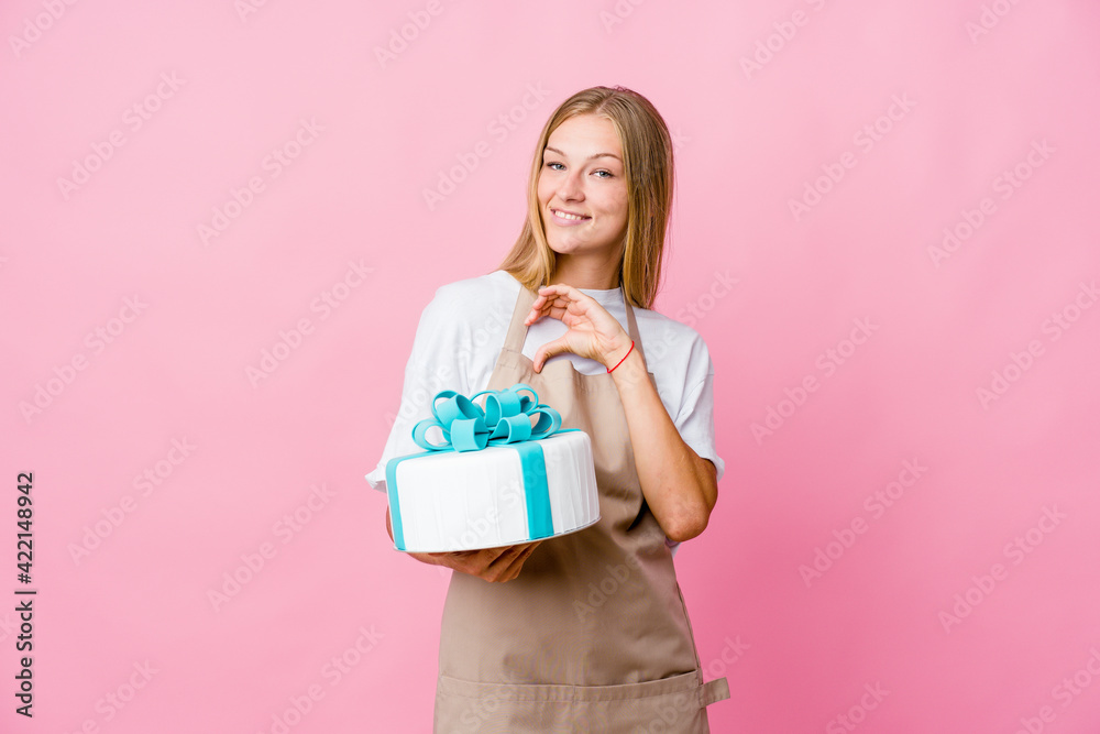 Young russian baker woman holding a delicious cake smiling and showing a heart shape with hands. Young russian baker woman holding a delicious cake smiling and showing a heart shape with hands.
