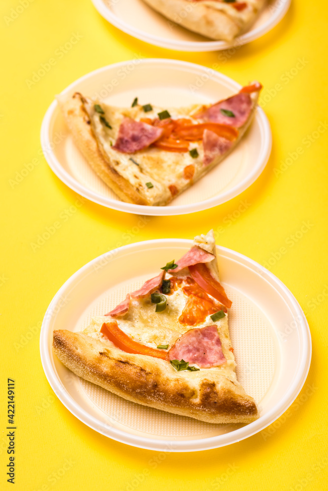 Takeaway and delivery. Three pieces of pizza in disposable plastic plates on a yellow background. Lunch for a group of friends. Vertical view Takeaway and delivery. Three pieces of pizza in disposable plastic plates on a yellow background. Lunch for a group of friends. Vertical view
