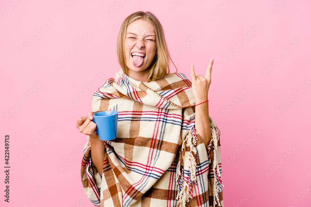 Young russian woman wrapped in a blanket drinking coffee showing rock gesture with fingers Young russian woman wrapped in a blanket drinking coffee showing rock gesture with fingers