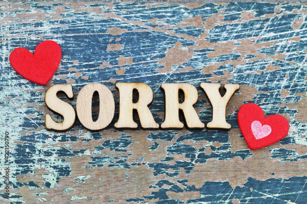 Sorry written with wooden letters on rustic surface with two red hearts