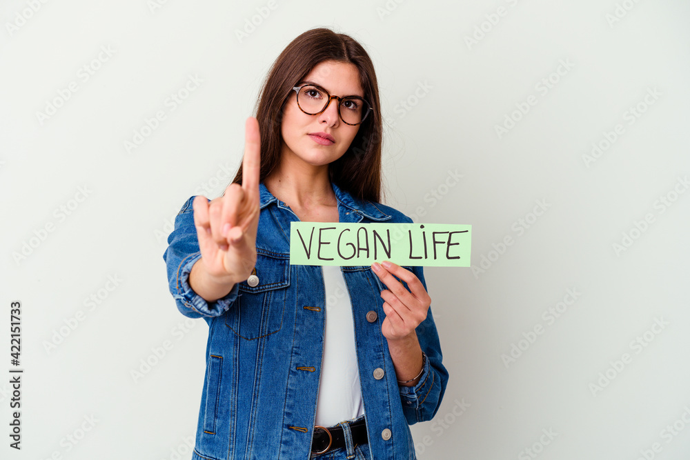 Young caucasian woman holding a vegan life placard isolated on white background smiling and pointing aside, showing something at blank space.