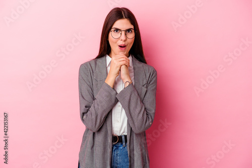 Young caucasian business woman isolated on pink background praying for luck, amazed and opening mouth looking to front. © Asier