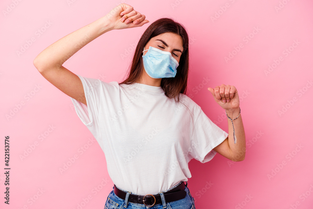 Young caucasian woman wearing a mask for virus isolated on pink background celebrating a special day, jumps and raise arms with energy. Young caucasian woman wearing a mask for virus isolated on pink background celebrating a special day, jumps and raise arms with energy.