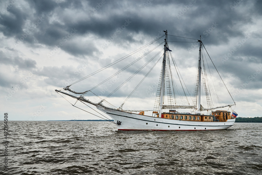 Antique sailing frigate of white color to the sea, the lowering storm sky, sails are lowered, masts and ropes