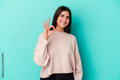 Young caucasian woman isolated on blue background cheerful and confident showing ok gesture.