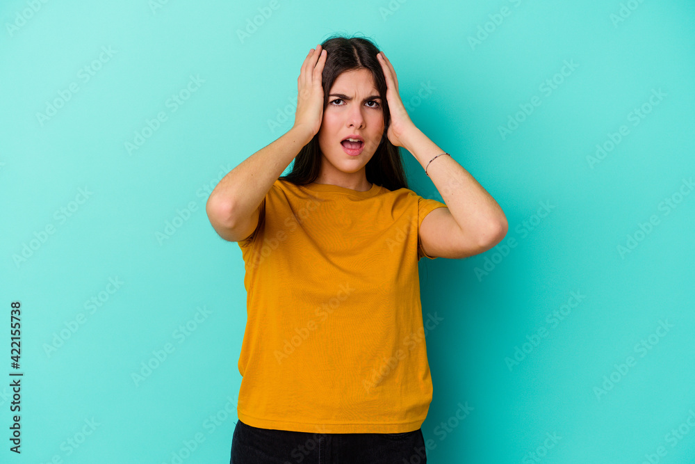 Young caucasian woman isolated on blue background covering ears with hands trying not to hear too loud sound. Young caucasian woman isolated on blue background covering ears with hands trying not to hear too loud sound.