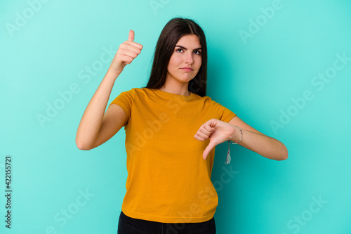 Young caucasian woman isolated on blue background showing thumbs up and thumbs down, difficult choose concept