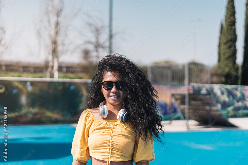 Portrait of a young African American girl smiling in yellow t-shirt and sunglasses with headphones hanging from her neck.
