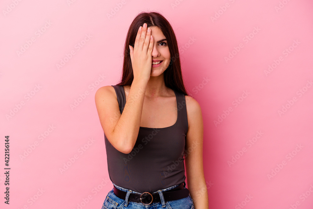 Young caucasian woman isolated on pink background having fun covering half of face with palm.