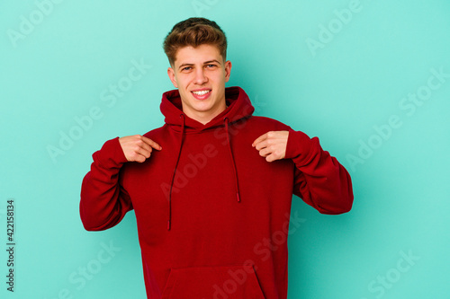 Young caucasian man isolated on blue background surprised pointing with finger, smiling broadly.