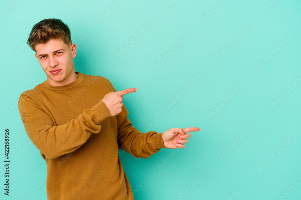 Young caucasian man isolated on blue background pointing with forefingers to a copy space, expressing excitement and desire.