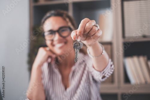 Focus on bunch of keys from house flat apartment in hand of smiling female. Blurred portrait of confident woman professional realtor offering new dwelling real estate unit to potential buyer. Close up photo