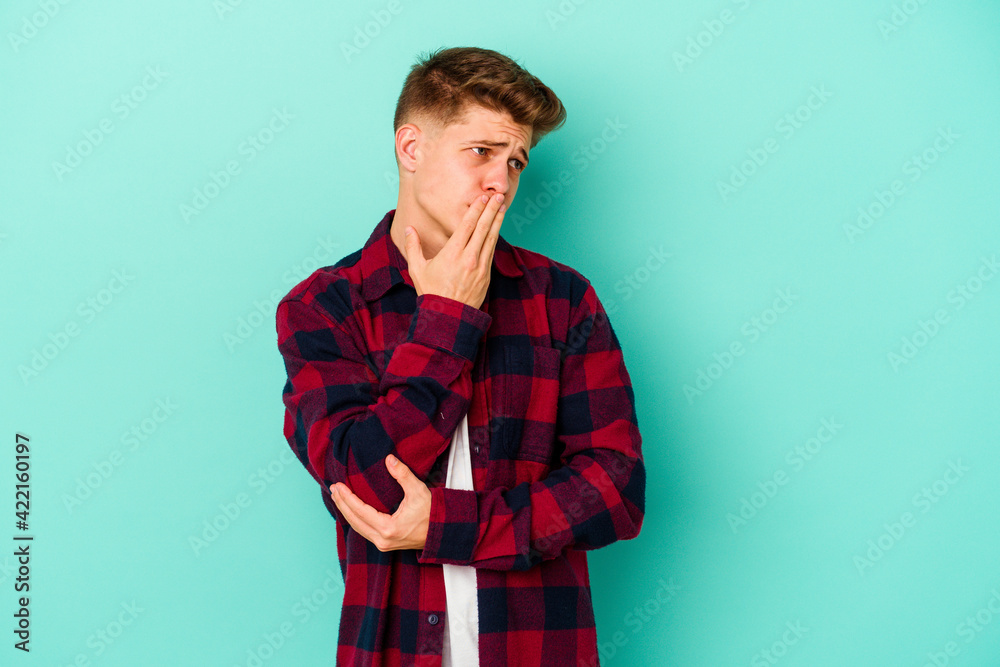 Young caucasian man isolated on blue background yawning showing a tired gesture covering mouth with hand. Young caucasian man isolated on blue background yawning showing a tired gesture covering mouth with hand.