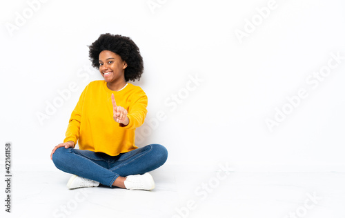 Young African American woman sitting on the floor showing and lifting a finger © luismolinero