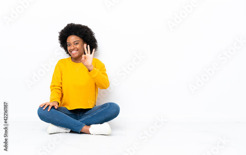 Young African American woman sitting on the floor happy and counting three with fingers © luismolinero