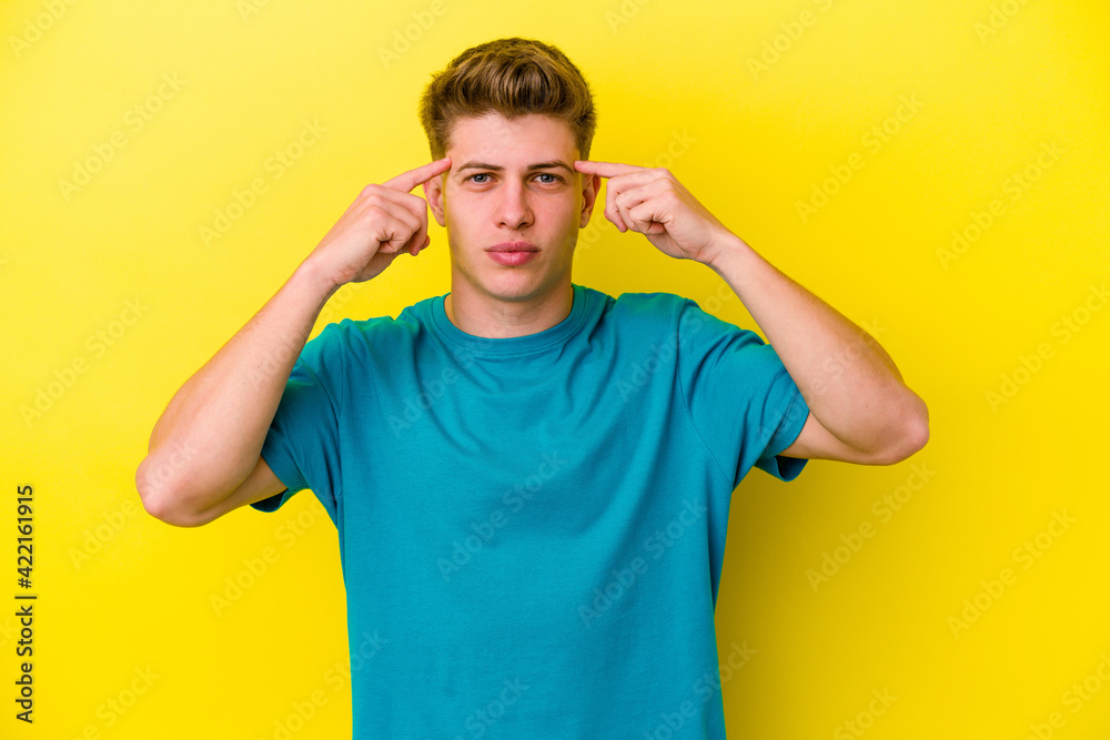 Young caucasian man isolated on yellow background focused on a task, keeping forefingers pointing head. Young caucasian man isolated on yellow background focused on a task, keeping forefingers pointing head.