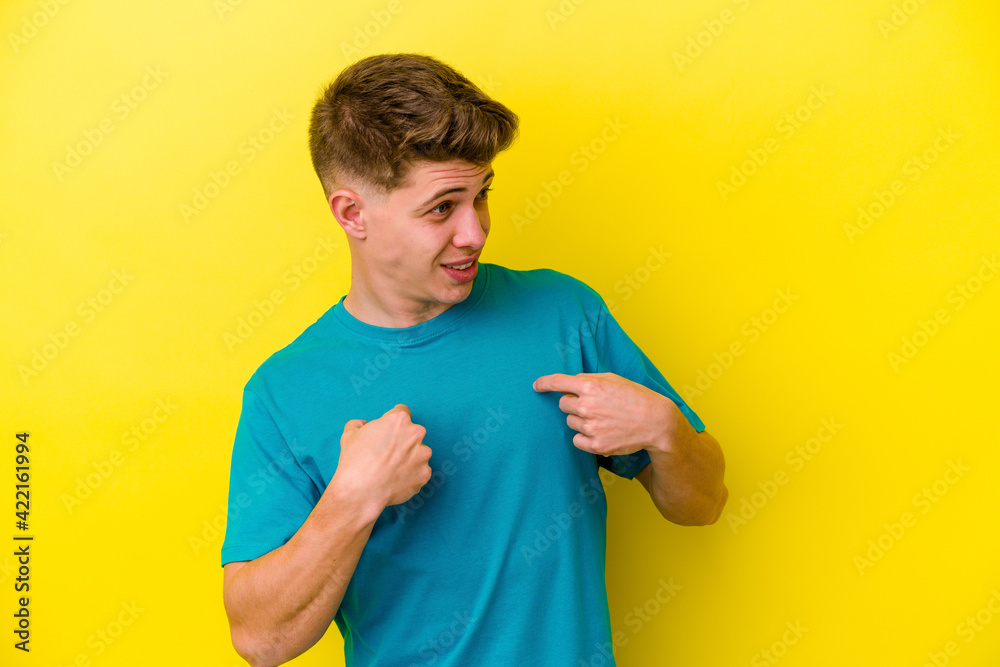 Young caucasian man isolated on yellow background surprised pointing with finger, smiling broadly.