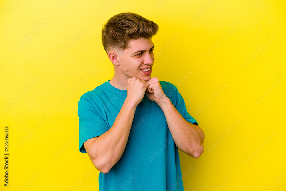 Young caucasian man isolated on yellow background keeps hands under chin, is looking happily aside. Young caucasian man isolated on yellow background keeps hands under chin, is looking happily aside.