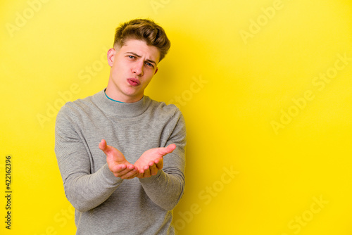 Young caucasian man isolated on yellow background folding lips and holding palms to send air kiss.