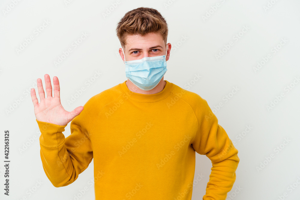 Young man wearing a mask for coronavirus isolated on white background smiling cheerful showing number five with fingers. Young man wearing a mask for coronavirus isolated on white background smiling cheerful showing number five with fingers.