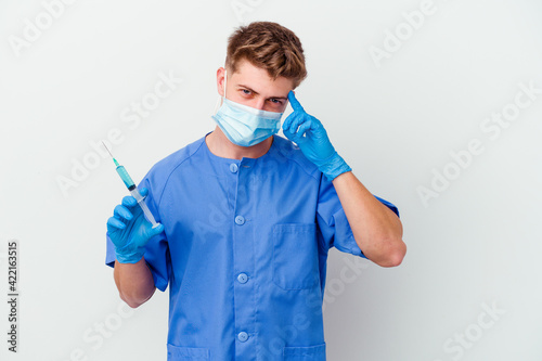 Young caucasian nurse man prepared to give a vaccine isolated on white background pointing temple with finger  thinking  focused on a task.