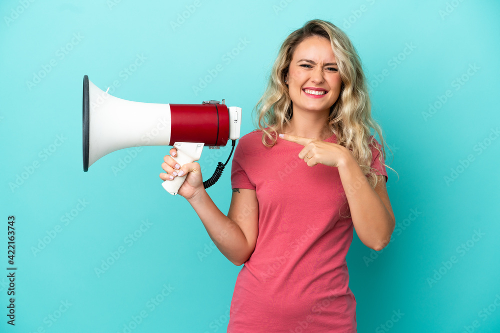 Young Brazilian woman isolated on blue background holding a megaphone and pointing side Young Brazilian woman isolated on blue background holding a megaphone and pointing side