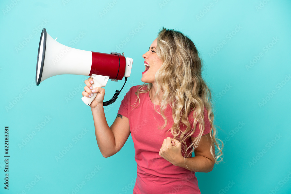 Young Brazilian woman isolated on blue background shouting through a megaphone to announce something in lateral position Young Brazilian woman isolated on blue background shouting through a megaphone to announce something in lateral position