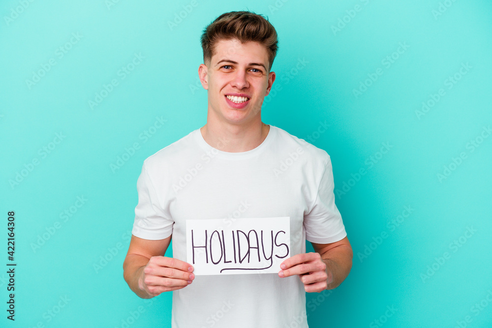 Young caucasian man holding a Holidays placard isolated on blue background Young caucasian man holding a Holidays placard isolated on blue background