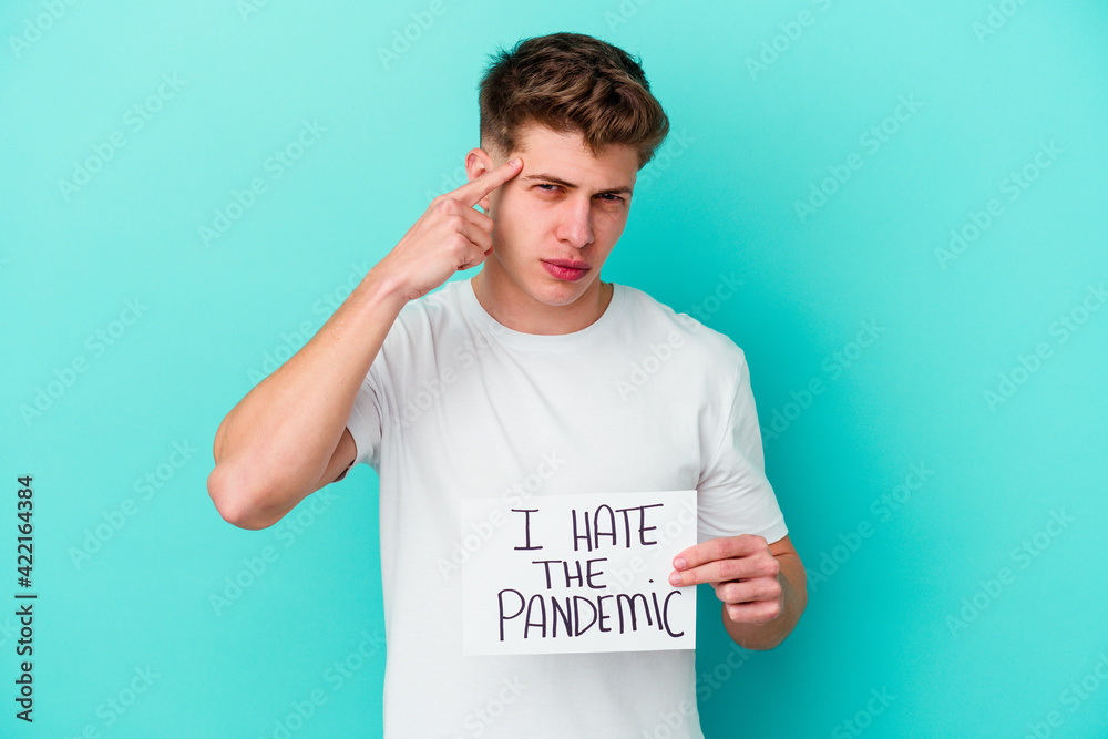 Young caucasian man holding a I hate the pandemic placard isolated on blue background Young caucasian man holding a I hate the pandemic placard isolated on blue background