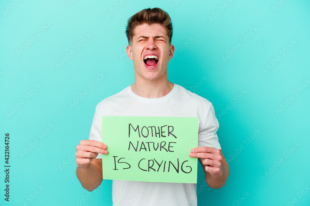 Young caucasian man holding a Mother Nature is crying placard isolated on blue background Young caucasian man holding a Mother Nature is crying placard isolated on blue background