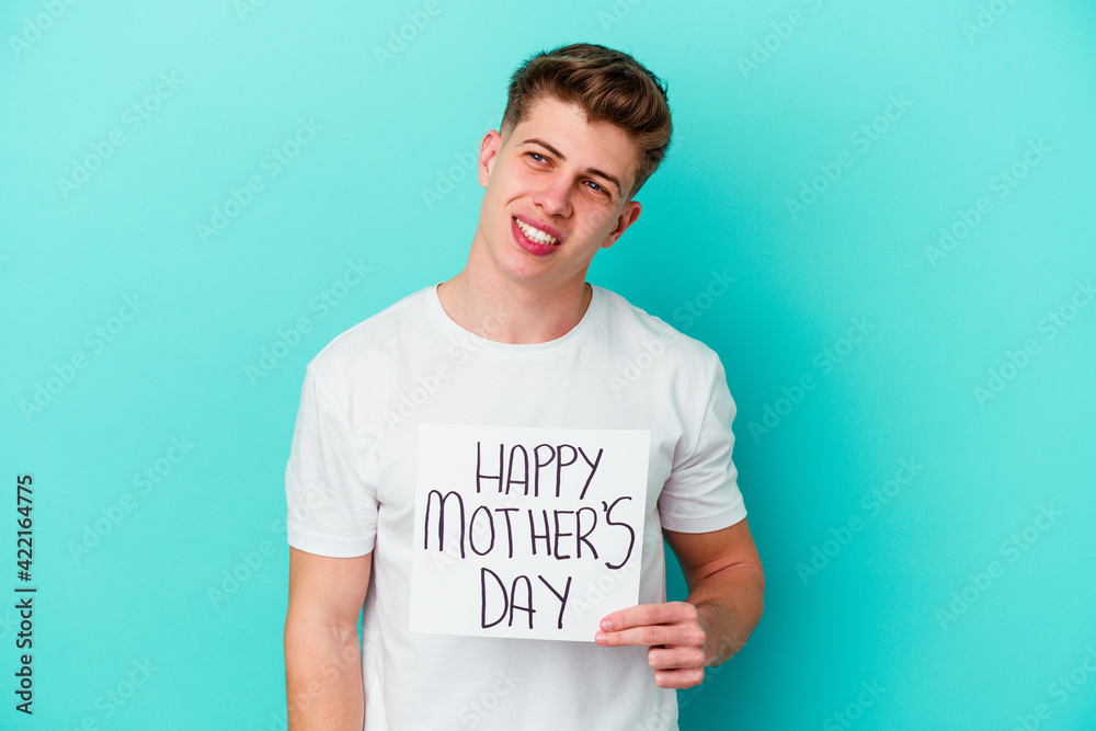 Young caucasian man holding a Happy Mothers day placard isolated on blue background Young caucasian man holding a Happy Mothers day placard isolated on blue background