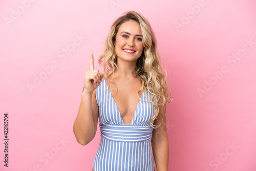 Young Brazilian woman in swimsuit in summer holidays isolated on pink background showing and lifting a finger in sign of the best