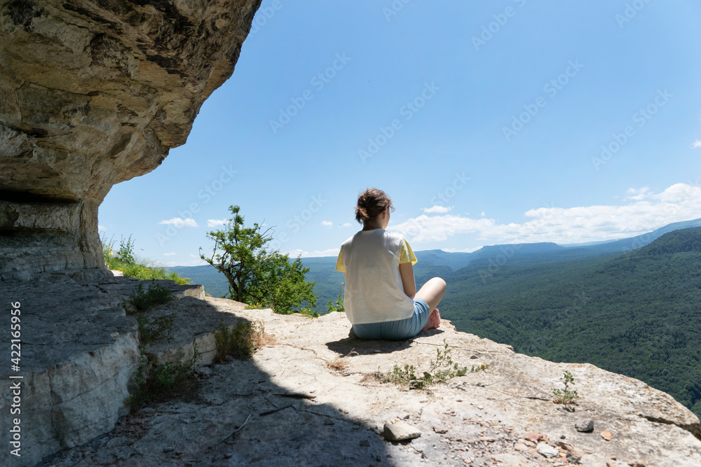 Young female sit on rock in high green mountains looking over green forest. Freedom concept, relaxation. Hiking in beautiful places, copy space.