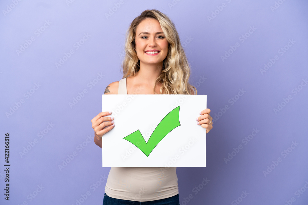 Naklejka premium Young Brazilian woman isolated on purple background holding a placard with text Green check mark icon with happy expression
