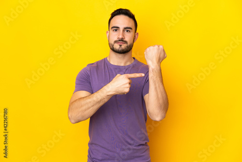 Young caucasian handsome man isolated on yellow background making the gesture of being late