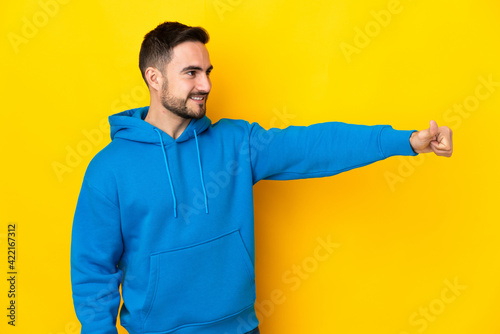 Young caucasian handsome man isolated on yellow background giving a thumbs up gesture © luismolinero