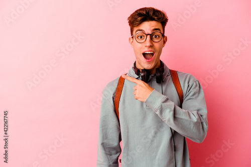 Young student man isolated on pink background pointing to the side