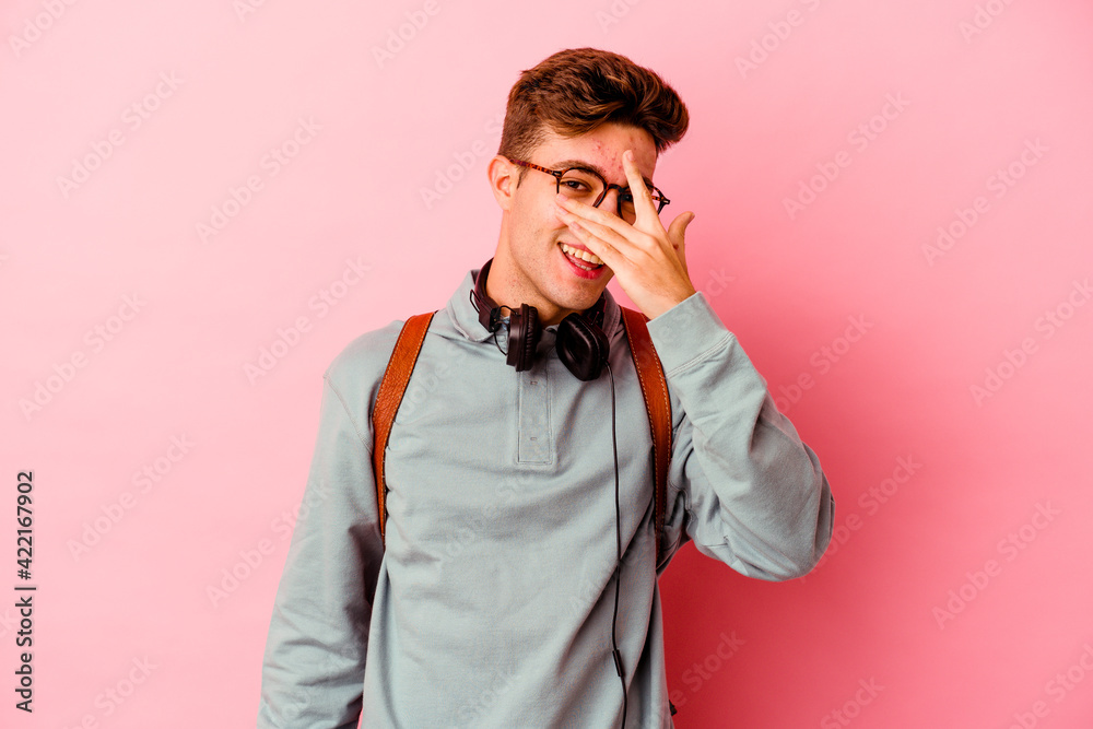 Young student man isolated on pink background blink at the camera through fingers, embarrassed covering face.