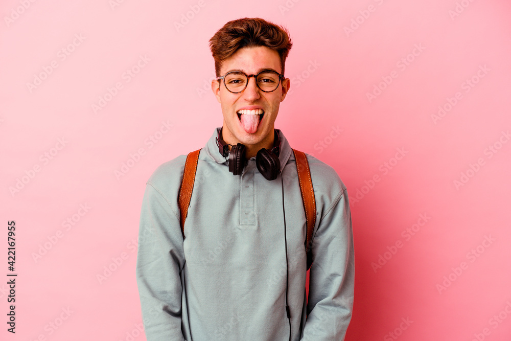 Young student man isolated on pink background funny and friendly sticking out tongue.