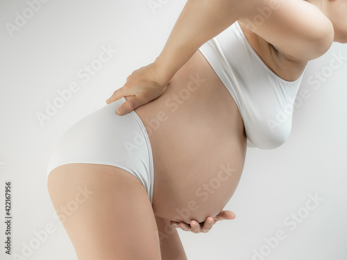 Pregnant woman suffering back ache. Lady in the third trimester of pregnancy. A pregnant woman in white underwear grabbed her belly and lower back white background. The girl in the last month of