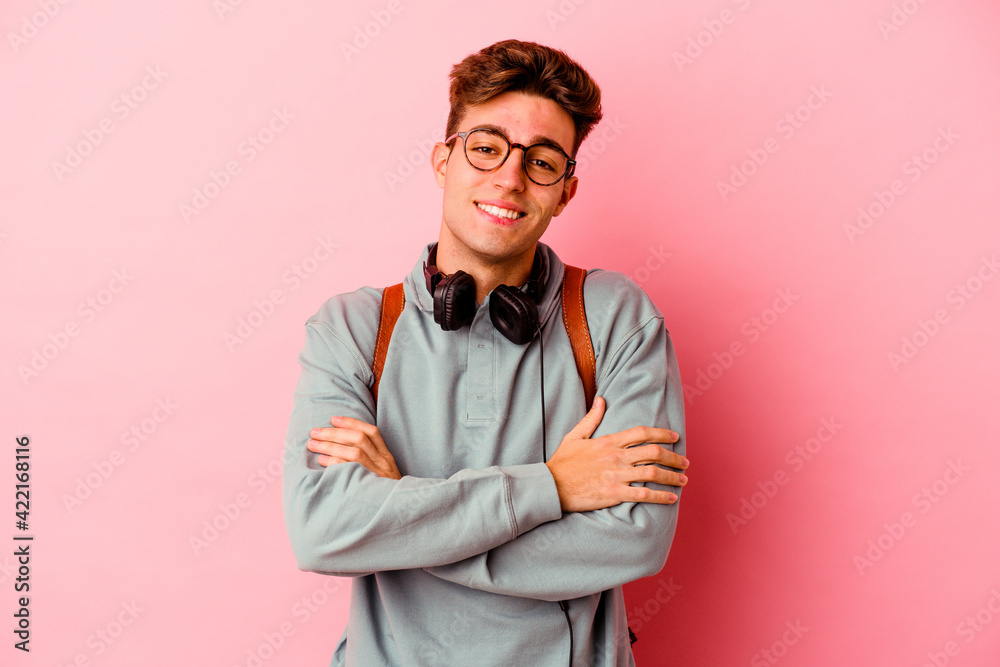 Young student man isolated on pink background who feels confident, crossing arms with determination. Young student man isolated on pink background who feels confident, crossing arms with determination.