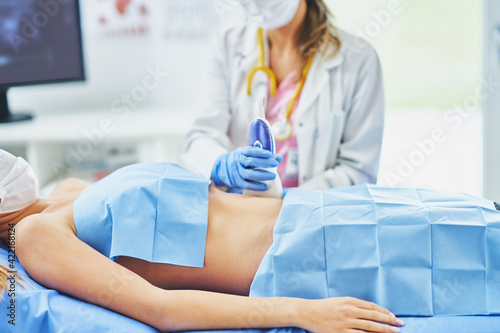 Doctor in mask doing ultrasound abdomen test to female patient