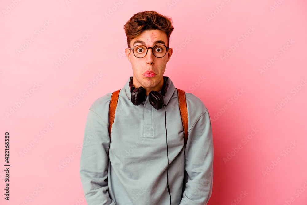 Fototapeta premium Young student man isolated on pink background shrugs shoulders and open eyes confused.