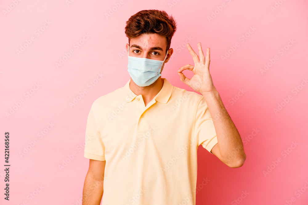 Young caucasian man wearing a protection for coronavirus isolated on pink background cheerful and confident showing ok gesture. Young caucasian man wearing a protection for coronavirus isolated on pink background cheerful and confident showing ok gesture.
