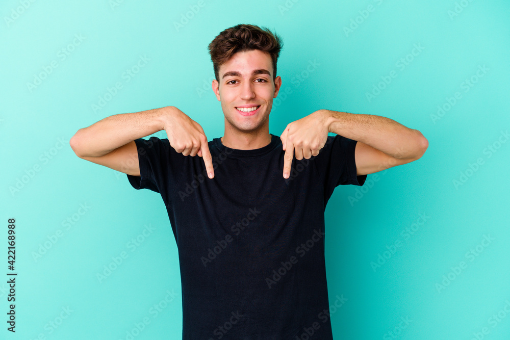 Young caucasian man isolated on blue background points down with fingers, positive feeling. Young caucasian man isolated on blue background points down with fingers, positive feeling.