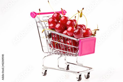 A supermarket cart is filled with ripe red cherries on a white background.