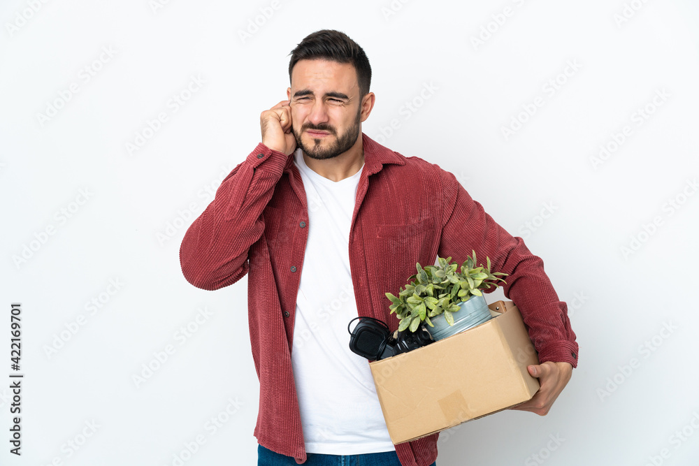 Young caucasian man making a move while picking up a box full of things isolated on white background frustrated and covering ears